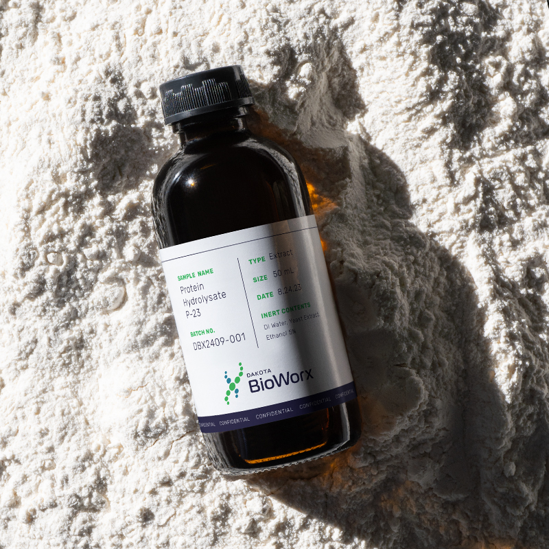 Dakota BioWorx product sample bottle labeled Protein Hydrolysate P-23, photographed on a white powder surface.